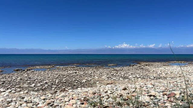 View of Issyk-Kul mountain lake, Kyrgyzstan. Waves splash on a sandy beach with rocks. Calm, peaceful natural background. Lake with a view of the Tien Shan Mountains. Kyrgyzstan 4K