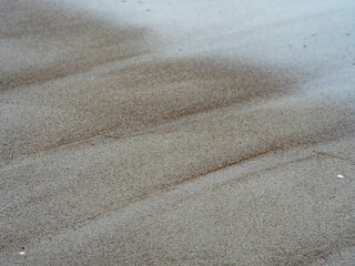 Nahaufnahme Sandstrand mit ablaufendem Wasser bei trüben Wetter