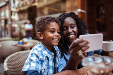 Smiling mother sitting in public cafe with son taking selfie