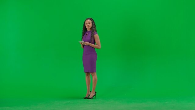 Female in dress isolated on chroma key green screen background. Full shot african american woman tv news host standing talking looking at camera.