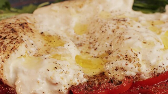 Burrata or Mozzarella cheese on fresh tomatoes and green arugula on plate close-up. From Italian cow's milk cheese made from mozzarella and cream.The outer casing is solid