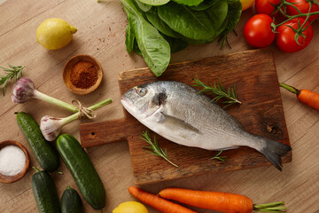 Raw sea bream fish on wooden board with vegetables - 773346231