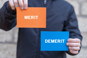 Man holding multi-colored paper cards sees inscription: MERIT DEMERIT. Demerit and merit...