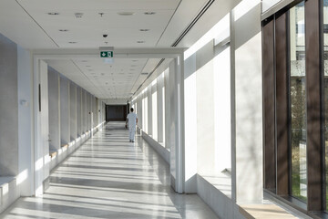 A medical worker walks along a long white corridor in a hospital