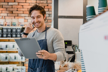 Cheerful young good-looking barista bartender shop owner assistant talking on phone holding folder...