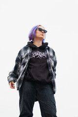 Young woman with colorfull blue hair, piercings and sunglasses posing. Wearing flannel and hoodie. Urban background.