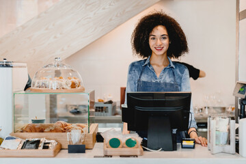 Confident young smiling african shop assistant vendor barista bartender waitress standing at cafe...