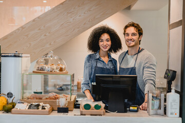 Two 20s multiethnic cafeteria workers standing at the cafe counter and selling food and drinks together. Teamwork and small business concept. Shop ownership