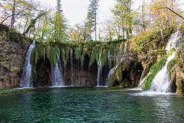 Scenic view of majestic waterfall Mali Prstavac in magical Plitvice lakes National Park, Karlovac, Croatia, Europe. Misty autumn landscape. Cascades overgrown by greenery flowing in emerald green pond