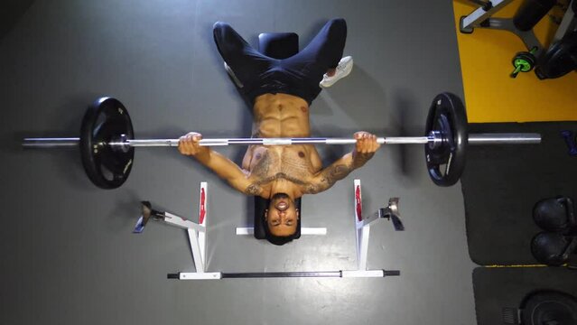 Strong black sportsman doing bench press workout with a barbell at sport club. Muscular athlete doing weightlifting exercises at modern gym. Healthy and active lifestyle concept. Top view