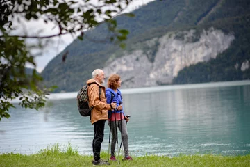 Gordijnen Portrait of beautiful active elderly couple hiking together in autumn mountains. Senior tourists looking at lake. © Halfpoint