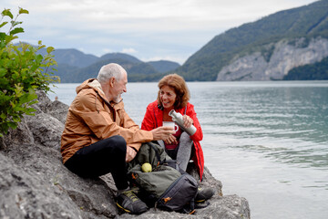 Active elderly couple hiking together in mountains. Drinking coffee and having healthy snack, to...
