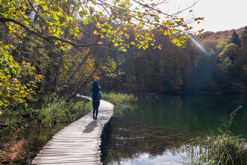 Hiker woman with baby carrier on enchanting hiking trail on rustical wooden footpath in Plitvice lakes National Park, Karlovac, Croatia, Europe. Walking over turquoise water in idyllic paradise nature