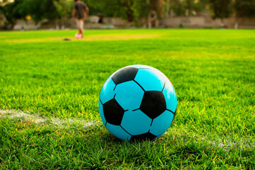 Imagen horizontal de una pelota de color azul de futbol Soccer al fondo personas practicando  - obrazy, fototapety, plakaty