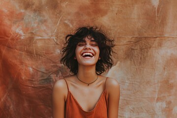 Joyful young woman laughing with closed eyes against a textured terracotta background.