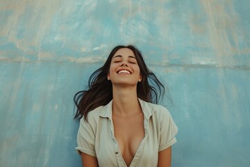 Joyful young woman laughing with closed eyes against a textured blue background, expressing happiness and carefree attitude.