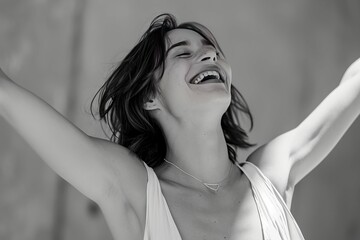 Joyful young woman laughing with arms raised in a candid black and white portrait.
