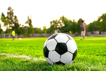 Imagen horizontal de un balón de futbol Soccer blanco con negro y al fondo dos personas...