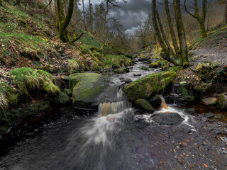 Mountain river in England, dreamy scenery, moss-covered stones and beautiful waterfall in the forest. Sunny creek in spring cloudy Yorkshire evening. small cascade surrounded by moss and autumn leaves