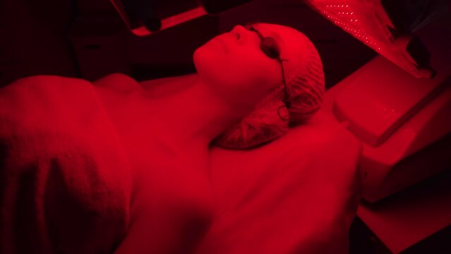 LED red cosmetic light is treating the facial skin of a young woman.
