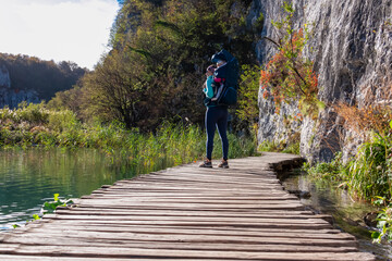 Hiker woman with baby carrier on enchanting hiking trail on rustical wooden footpath in Plitvice...