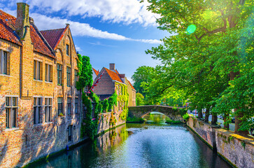 Meebrug stone bridge across Groenerei Green Canal water, embankment of Reie river with trees and plants in Brugge old town, medieval buildings in Bruges city historic centre, Flemish Region, Belgium - obrazy, fototapety, plakaty