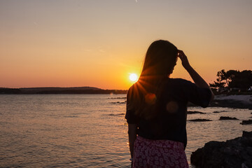 Fototapeta premium Silhouette of woman with on idyllic beach at romantic sunset in Medulin, Istria peninsula, Croatia. Sunglitter on calm water surface of Adriatic Mediterranean Sea, Kvarner Gulf in summer. Dramatic sky