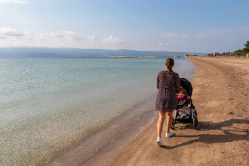 Loving mother with baby stroller walking on idyllic sand beach in coastal town Omis, Split-Dalmatia, South Croatia, Europe. Majestic coastline of Omis Riviera, Adriatic Sea in Balkans. Family travel