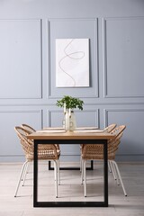 Rattan chairs, table, burning candles and vase with green branches in stylish dining room