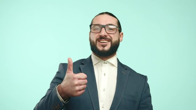 Bearded man in a suit making a thumbs-up gesture, encouraging likes and follows, against a light turquoise backdrop. Ideal for promotional and advertising material. Camera 8K RAW. 