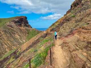 Obraz premium Hiker woman on idyllic hiking trail along rocky rugged cliffs at Ponta de Sao Lourenco peninsula, Canical, Madeira island, Portugal, Europe. Rugged terrain of coastline of Atlantic Ocean. Wanderlust