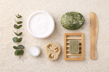 Flat lay composition with moisturizing cream in open jar and other body care products on light textured table