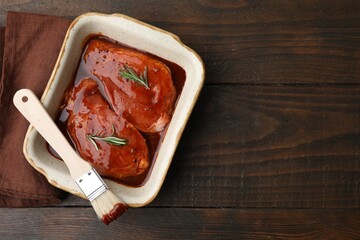 Raw marinated meat, rosemary and basting brush on wooden table, top view. Space for text