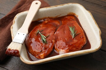 Raw marinated meat, rosemary and basting brush on wooden table, closeup
