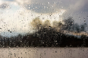 Raindrops on a window with a defocused lake landscape in the background, in the afternoon in the...