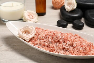Natural sea salt in bowl, spa stones, roses and candle on wooden table