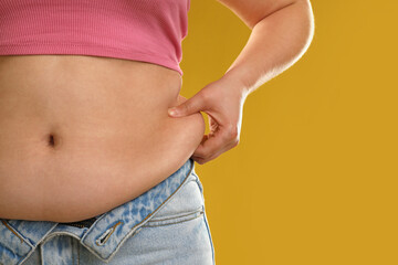 Woman touching belly fat on goldenrod background, closeup. Overweight problem - obrazy, fototapety, plakaty