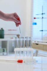 Laboratory analysis. Woman dripping liquid into test tubes at white table indoors, closeup