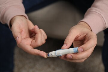 Diabetes test. Man checking blood sugar level with lancet pen on blurred background, closeup