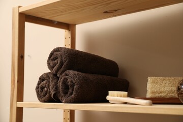 Soft towels, brush and loofah on wooden shelf indoors, closeup