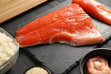 Making sushi rolls. Fresh salmon and other ingredients on black wooden table, closeup