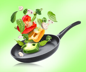 Frying pan with fresh ingredients in air on green background