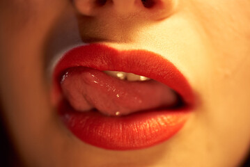 Female mouth with red lipstick. The girl sexually licks her lips in red lipstick with her tongue.