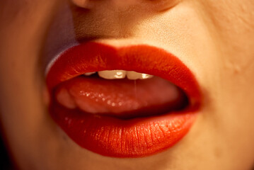 Female mouth with red lipstick. The girl sexually licks her lips in red lipstick with her tongue. - obrazy, fototapety, plakaty