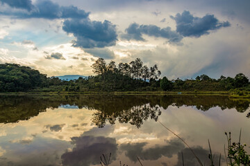 A forest on a hill in the eastern Andean mountains of central Colombia reflected in the calm water of a lagoon, at sunset.