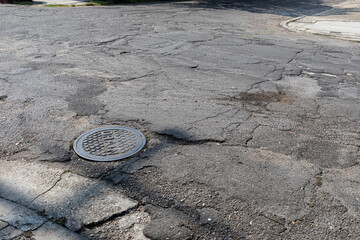 Undulating asphalt with patch layers crumbling, manhole drain creative copy space for...