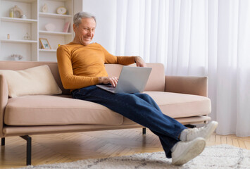 Relaxed elderly man working on laptop on couch