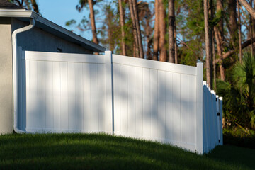 Fototapeta na wymiar White vinyl picket fence on green lawn surrounding property grounds for backyard protection and privacy