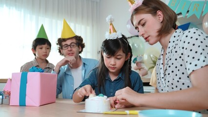 Caucasian mother cutting cake while family congratulate in girl's birthday. Diverse family...