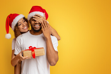 Black millennial couple with Christmas gift on orange background